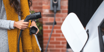 A woman is charging her electric car in front of a brick wall as part of the Lotus EV Venture.