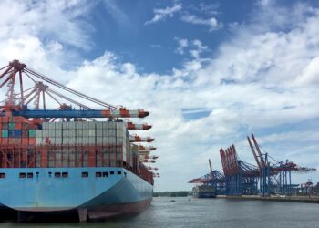 Container ship at port, loaded with cargo containers under large cranes. Challenging ocean market conditions. - Supply Chain News