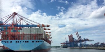 Container ship at port, loaded with cargo containers under large cranes. Challenging ocean market conditions. - Supply Chain News