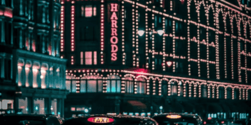 Night view of Harrods department store in London, illuminated with Christmas lights. Black cabs are parked in front. - Supply Chain News