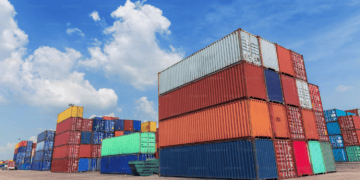 Stacked shipping containers at a port. Import/export logistics. - Supply Chain News