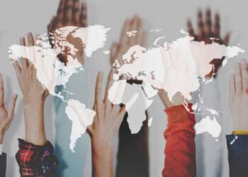 Diverse hands raised, superimposed on a world map, illustrating global collaboration during the COVID-19 pandemic. - Supply Chain News