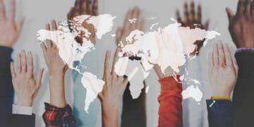 Diverse hands raised, superimposed on a world map, illustrating global collaboration during the COVID-19 pandemic. - Supply Chain News