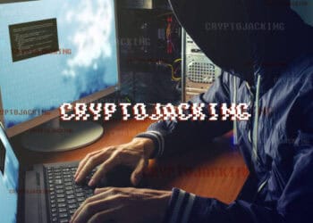 Hooded figure using computer, "Cryptojacking" displayed. Cryptocurrency scam warning. - Supply Chain News