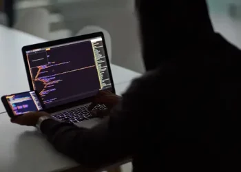 Person working on laptop and phone, reviewing code related to cybersecurity and supply chain risk management. - Supply Chain News