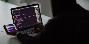 Person working on laptop and phone, reviewing code related to cybersecurity and supply chain risk management. - Supply Chain News