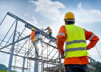 Construction workers on scaffolding assembling a metal framework. - Supply Chain News