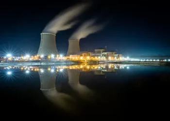 A nuclear power plant faces challenges and risks as it lights up at night, contributing to climate change.