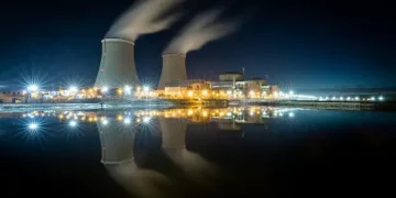 A nuclear power plant faces challenges and risks as it lights up at night, contributing to climate change.