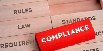 A red sign with the word compliance on top of a stack of wooden blocks, symbolizing labour law compliance.