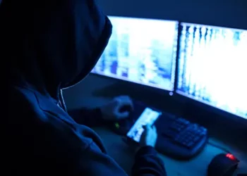 Hooded figure using computer, investigating potential gold bullion fraud. - Supply Chain News