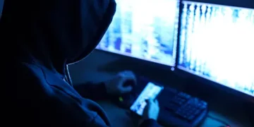 Hooded figure using computer, investigating potential gold bullion fraud. - Supply Chain News