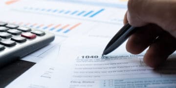 Close-up of a hand filling out a 1040 tax form with a pen. - Supply Chain News