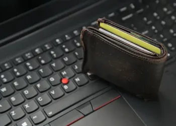 Brown leather wallet with credit cards on laptop keyboard; illustrating online fraud risk. - Supply Chain News