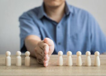 Person's hands reaching for small wooden figures representing Hong Kong officials facing potential sanctions. - Supply Chain News