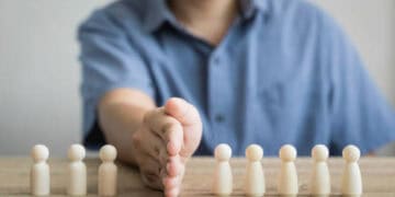 Person's hands reaching for small wooden figures representing Hong Kong officials facing potential sanctions. - Supply Chain News