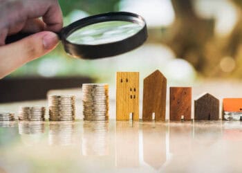 Wooden house models and stacks of coins under a magnifying glass. Impact of sanctions on Niger's currency. - Supply Chain News