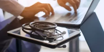 A doctor using a laptop to overcome macroeconomic challenges in the medtech industry while addressing staffing shortages.