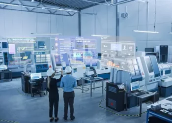 A group of people in a factory engaged in strategic manufacturing, examining machinery and discussing potential CPGs and M&A opportunities.