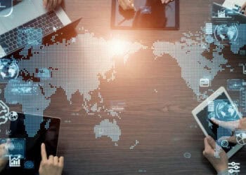 A group of people using laptops around a table with a world map, discussing the Global Economic Implications and Expansion opportunities for the BRICS countries.