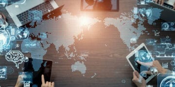 A group of people using laptops around a table with a world map, discussing the Global Economic Implications and Expansion opportunities for the BRICS countries.