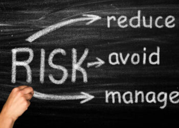 A hand drawing the words reduce and manage risk on a blackboard.