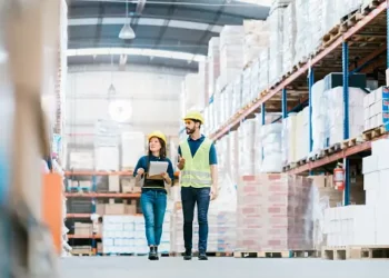 Two warehouse workers in hard hats review paperwork, showcasing efficient freight forwarding operations for 2023. - Supply Chain News