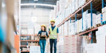 Two warehouse workers in hard hats walking through a warehouse to prepare for the holiday season.