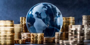 Glass globe on stacks of gold coins; global economic recovery. - Supply Chain News