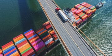 Aerial view of cargo ships and trucks on a bridge, illustrating global trade and economic activity. - Supply Chain News