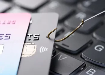 Credit cards and a phishing hook on a laptop keyboard; identity theft and credit card fraud. - Supply Chain News