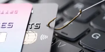 Credit cards and a phishing hook on a laptop keyboard; identity theft and credit card fraud. - Supply Chain News