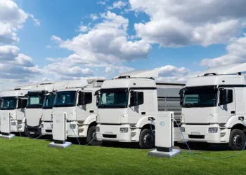 Row of electric delivery trucks charging at a station. Sustainable last-mile logistics. - Supply Chain News