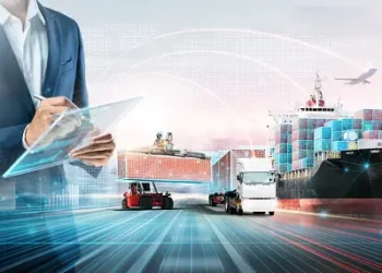 A man in a suit is holding a clipboard in front of a container ship, managing the supplier information within the supply chain.