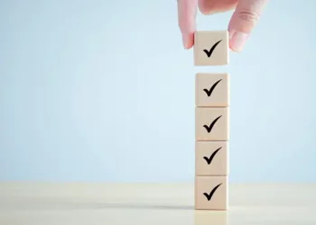 A hand carefully placing a cube on top of a stack of wooden blocks, symbolizing the importance of diversity and inclusion in procurement processes and supplier programs.