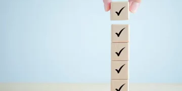 A hand carefully placing a cube on top of a stack of wooden blocks, symbolizing the importance of diversity and inclusion in procurement processes and supplier programs.