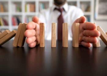 Hands stopping dominoes from falling; representing climate-related financial risk management. - Supply Chain News