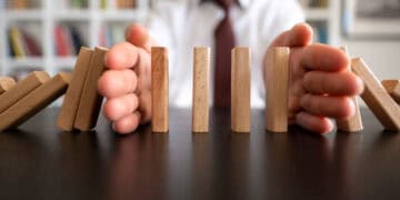 Hands stopping dominoes from falling; representing climate-related financial risk management. - Supply Chain News