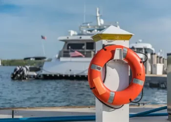 Orange life preserver on a dock with a yacht in the background. Maritime safety. - Supply Chain News