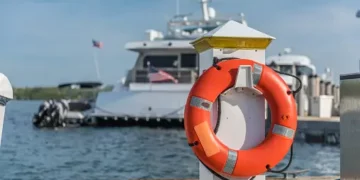 Orange life preserver on a dock with a yacht in the background. Maritime safety. - Supply Chain News