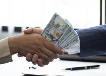 A Malaysian Deputy Prime Minister involved in corruption, depicted with a hand shaking hands with money.