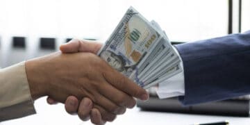 A Malaysian Deputy Prime Minister involved in corruption, depicted with a hand shaking hands with money.
