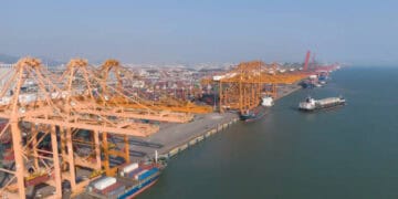 An aerial view of a large container ship docked at a port, promoting economic growth.