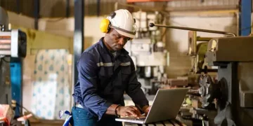 A man employing a strategic approach while working on a laptop in a manufacturing factory.