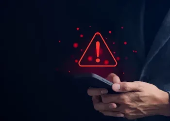 A businessman holding a smartphone with a red warning sign on it, signaling a cybersecurity incident for Molson Coors.