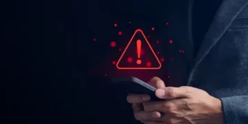 A businessman holding a smartphone with a red warning sign on it, signaling a cybersecurity incident for Molson Coors.