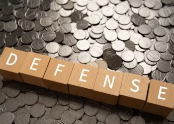 Wooden blocks spelling "DEFENSE" on a pile of coins. Japan's defense budget. - Supply Chain News