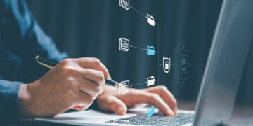 Person working on laptop, reviewing secure files. Enhanced KYC/AML protocols. - Supply Chain News