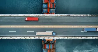 An aerial view of a container ship optimizing supply chain efficiency while crossing a bridge.