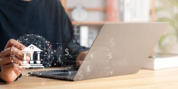 A man is using a laptop to participate in US-EU Trade Talks, while an image of money can be seen on the screen.